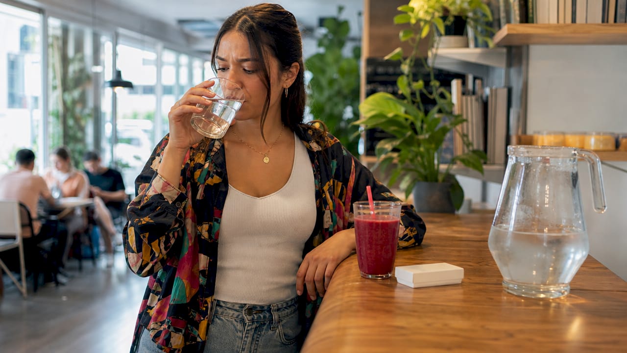 Woman drinking detox drink at kitchen table