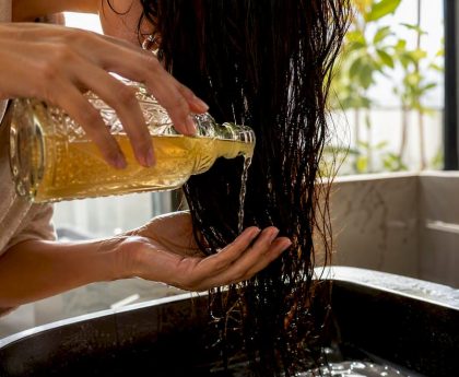 Hands pouring diluted apple cider vinegar rinse on hair
